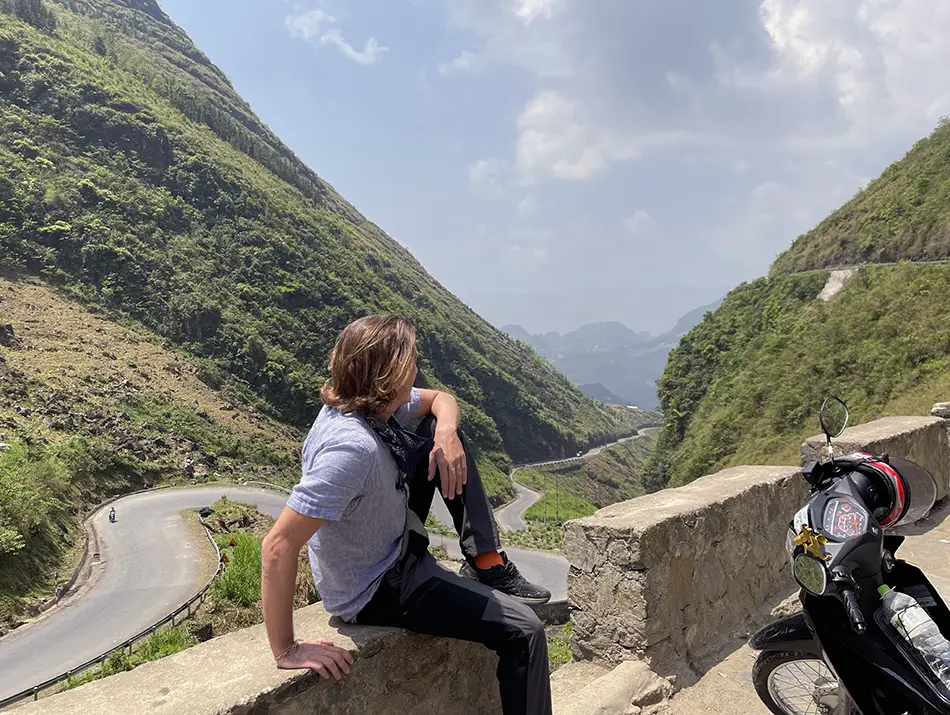 Yuriy Malykh resting on the Ha Giang Loop overlooking dramatic mountain scenery in northern Vietnam.