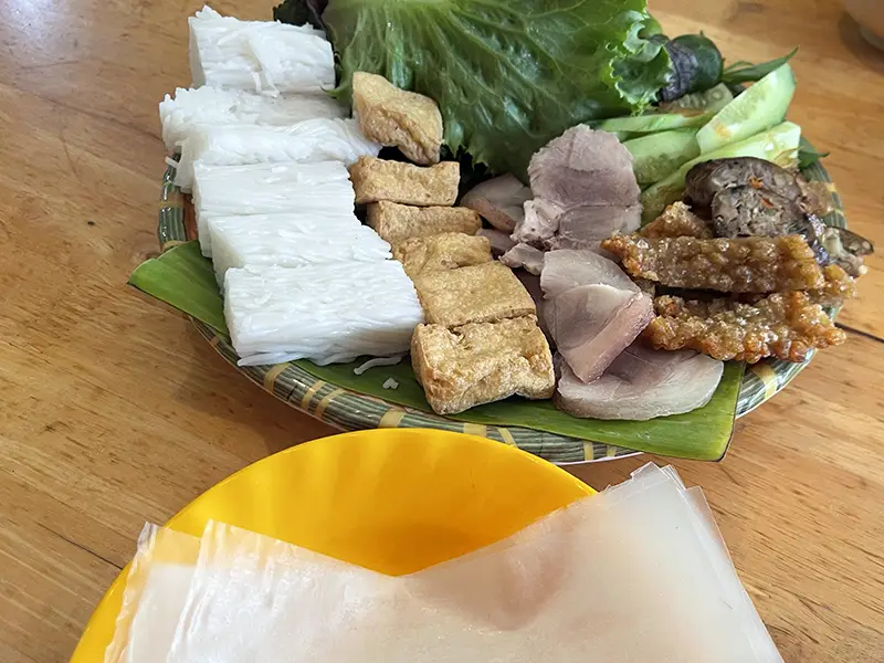 Traditional Vietnamese dish bun dau served on a tray with tofu, noodles, herbs, and fermented shrimp paste.