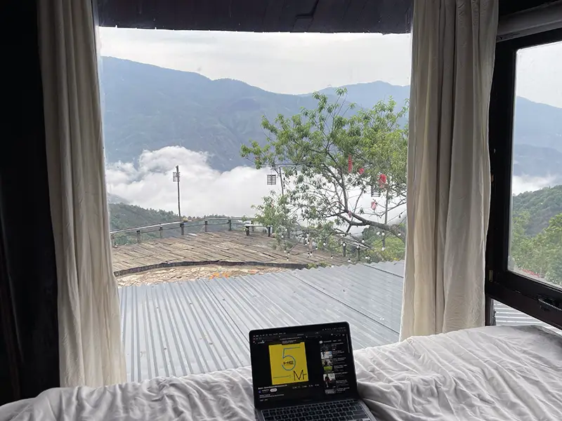 View of cloud-covered mountains through a glass window at a guesthouse in Ta Xua
