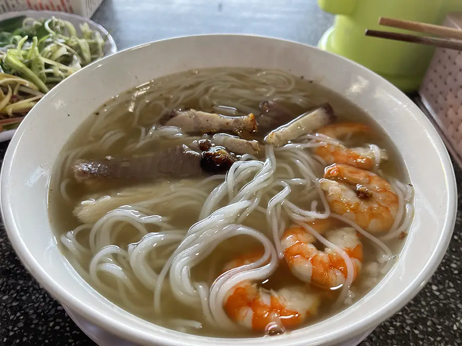 Bowl of Vietnamese seafood noodle soup with shrimp and fresh herbs, a typical local dish for travelers exploring Vietnam cuisine
