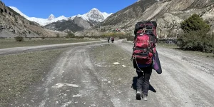 Traveler walking on a mountain road with an oversized backpack, illustrating overpacking mistakes to avoid with a travel planning checklist.