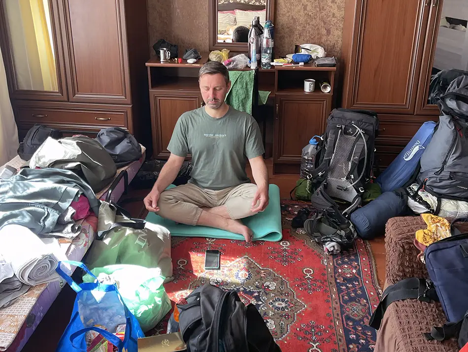Traveler meditating among packed bags in a room, highlighting mindful travel preparation and final trip organization before departure.