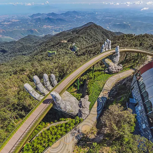 Aerial view of the Golden Bridge in Vietnam, curving across a mountain ridge and held by giant stone hands