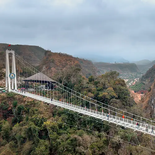 Full view of Bach Long Glass Bridge stretching across a deep valley in Moc Chau, with visitors walking across