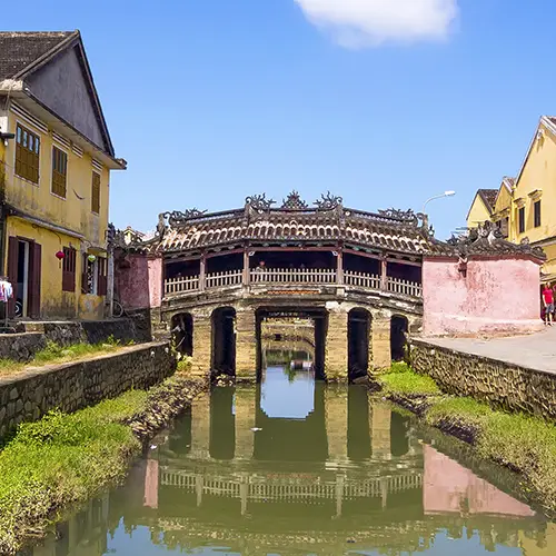 Daytime view of the Japanese Covered Bridge in Hoi An, with traditional houses and clear canal reflections