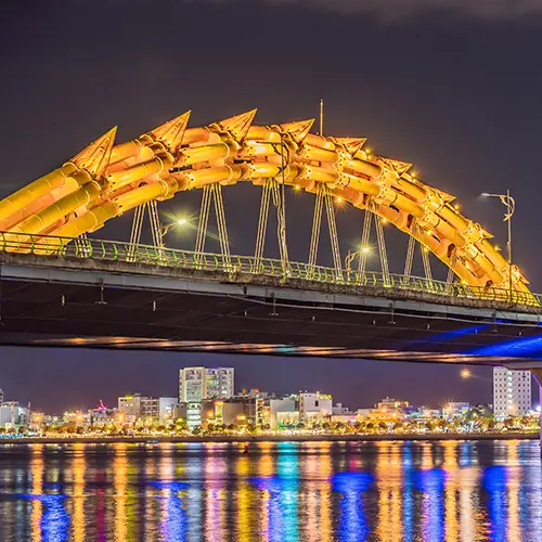 Night view of Dragon Bridge in Da Nang glowing over the Han River with city lights reflecting in the water