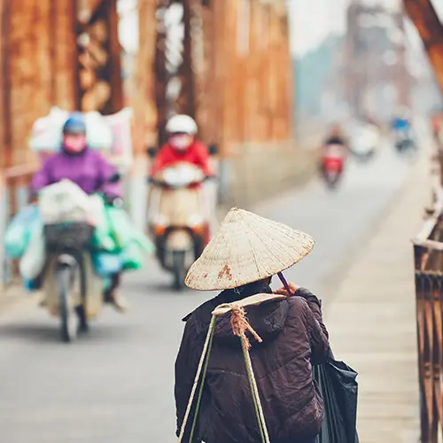 Vietnamese woman in conical hat walking on Long Bien Bridge alongside scooters and motorbikes in Hanoi