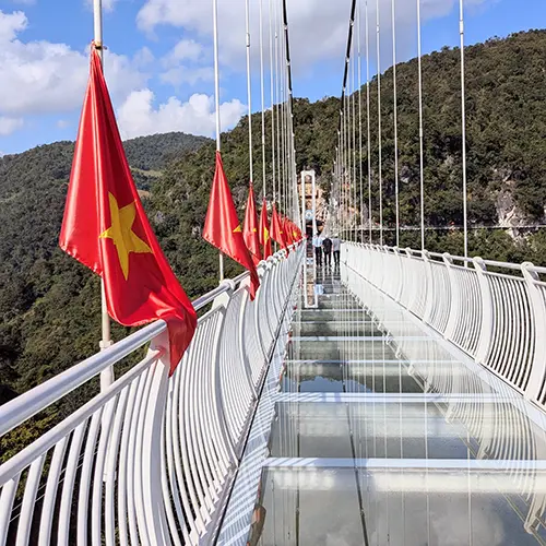 Close-up of Bach Long Glass Bridge walkway with Vietnamese flags and transparent glass panels above the valley