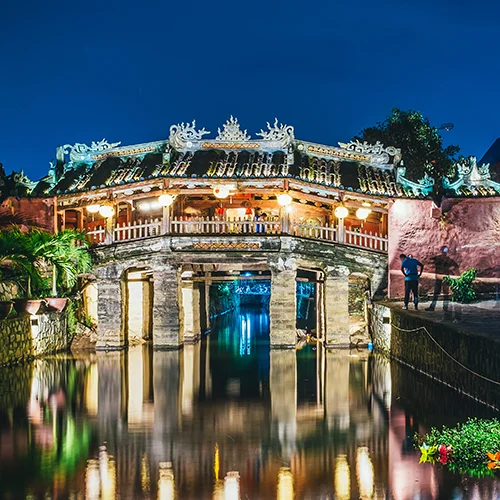 Japanese Covered Bridge in Hoi An illuminated at night, reflected in the canal with warm lights and detailed architecture