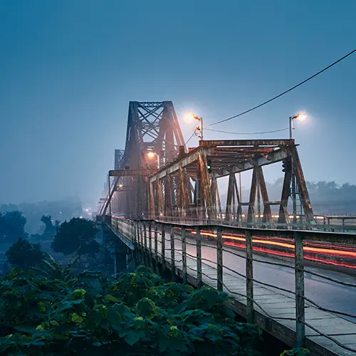 Long Bien Bridge in Hanoi at night with streetlights glowing and motion blur from passing traffic