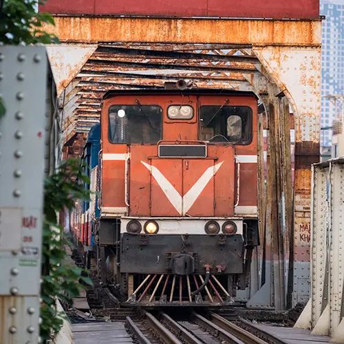 Front view of a red locomotive entering Long Bien Bridge in Hanoi, passing through a rusted steel frame