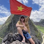 Traveler at mountain summit with Vietnam flag in Ha Giang, capturing the spirit of Vietnam hidden gems and remote adventure
