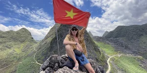 Traveler at mountain summit with Vietnam flag in Ha Giang, capturing the spirit of Vietnam hidden gems and remote adventure