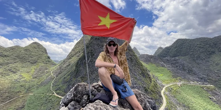 Traveler at mountain summit with Vietnam flag in Ha Giang, capturing the spirit of Vietnam hidden gems and remote adventure