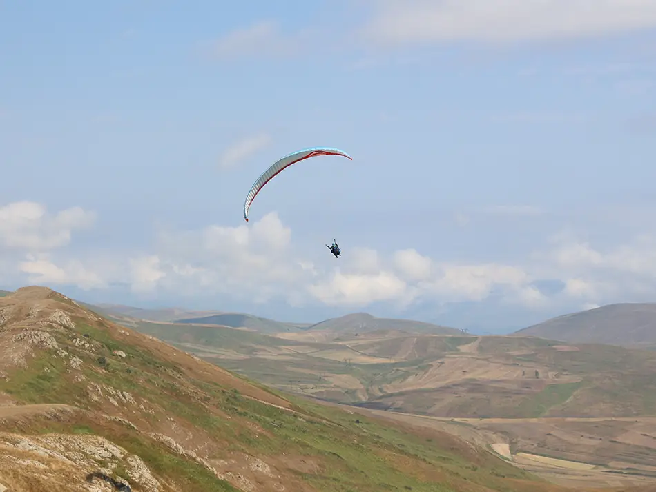 Paraglider flying above hills near Lake Sevan, a top Armenia adventure activity