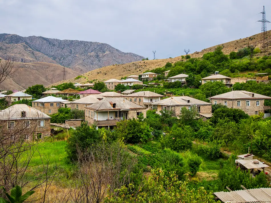 Village spreads across green orchards and hillside cottages under hazy mountains.