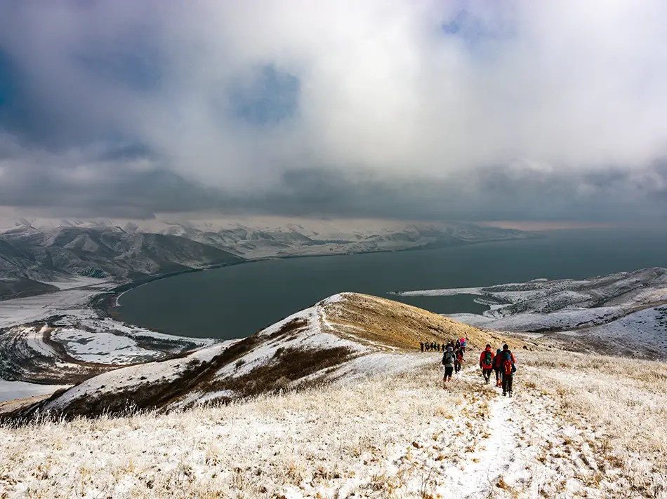 Hikers follow a snowy ridge on Mount Artanish above the lake
