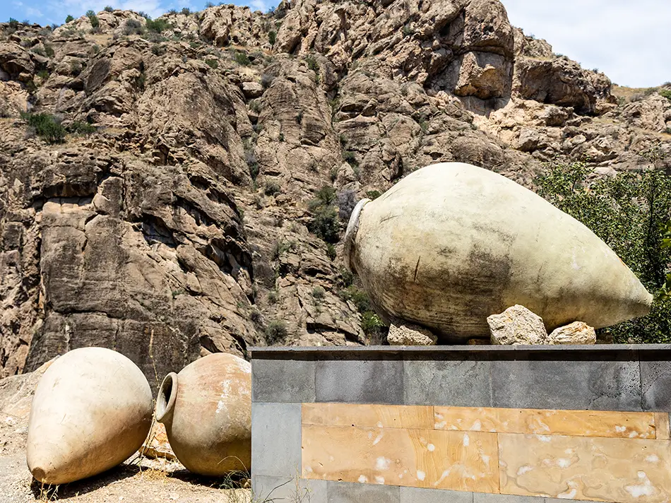 Giant clay wine vessels displayed against rugged canyon rocks near Areni.