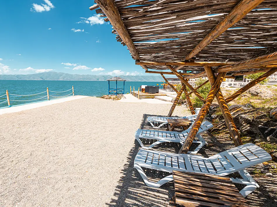Wooden shade cabanas and loungers line a sandy beach.
