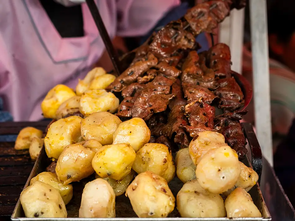 Beef heart anticuchos char-grilled with potato and corn, best food in Peru, on Lima street stalls.
