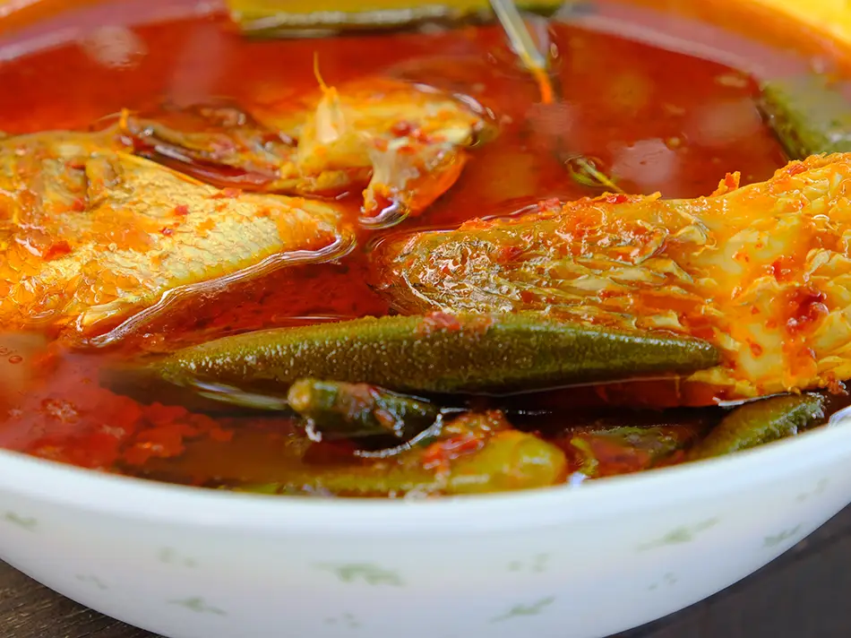 Spicy and sour asam pedas fish stew with tamarind broth and fresh herbs.