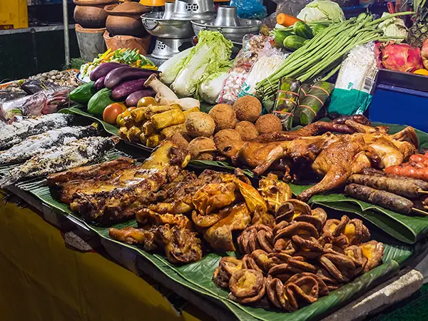 Best food in Laos: night market stall with grilled chicken, sausages, salt-crusted fish, fresh vegetables and seafood.
