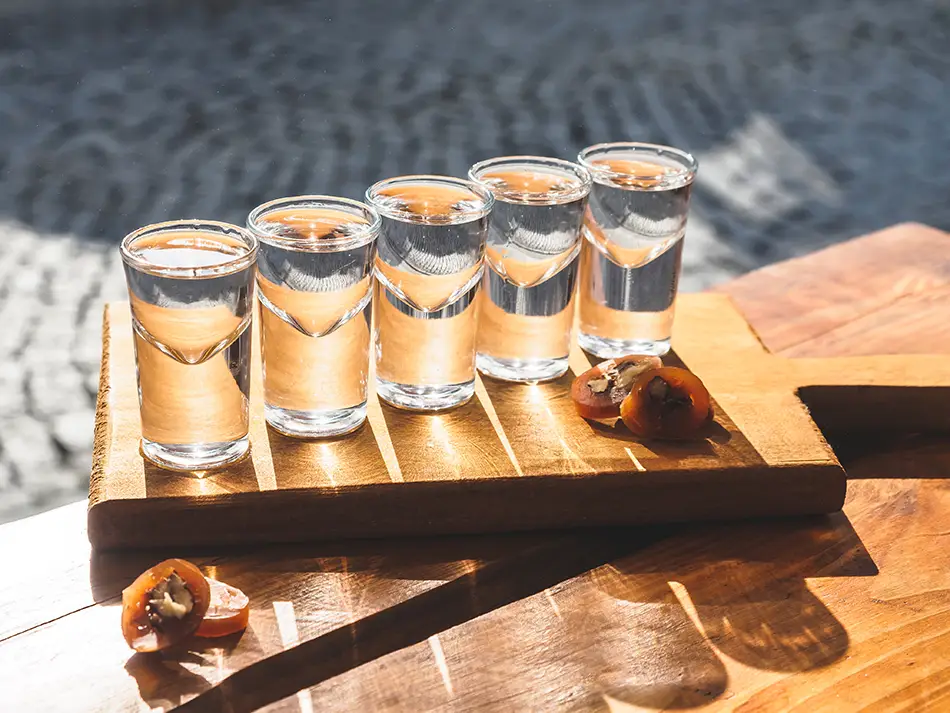Chacha tasting flight with small clear glasses on a wooden board.