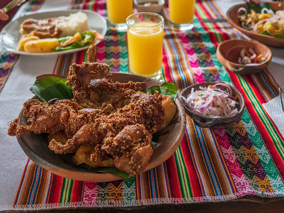Roasted cuy with blistered skin served beside potatoes and corn — iconic foods of Ecuador.