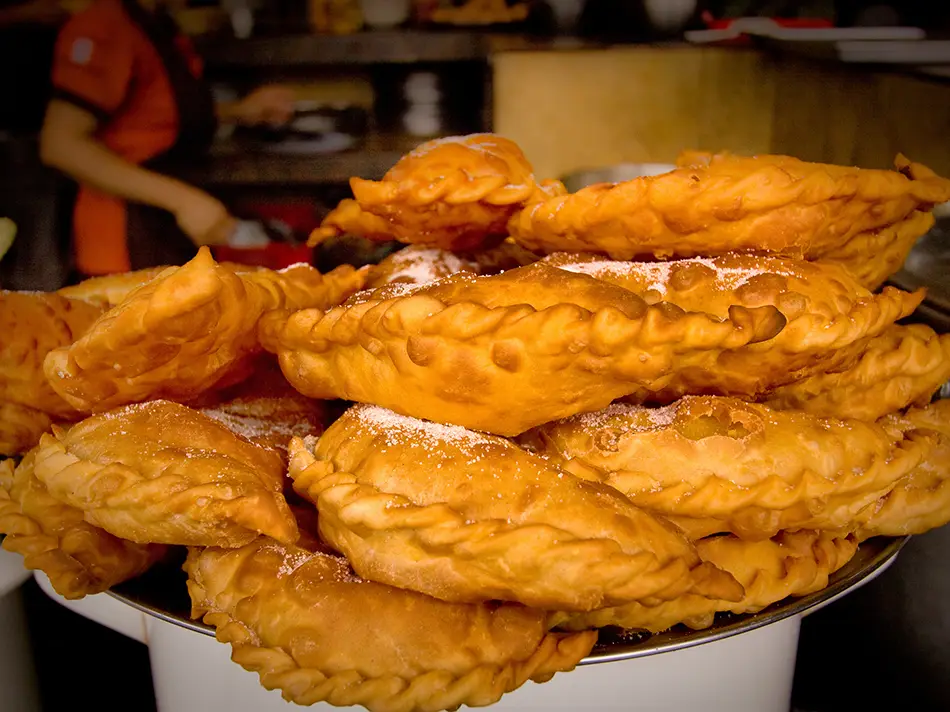 Sugar-dusted cheese empanadas stacked on a plate, their puffed shells just fried.