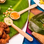Best food in Ecuador: overhead flat lay of fritada pork, llapingachos, mote with beans, and aji sauces on banana leaf.