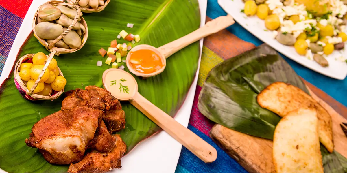 Best food in Ecuador: overhead flat lay of fritada pork, llapingachos, mote with beans, and aji sauces on banana leaf.