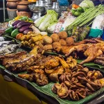 Best food in Laos: night market stall with grilled chicken, sausages, salt-crusted fish, fresh vegetables and seafood.