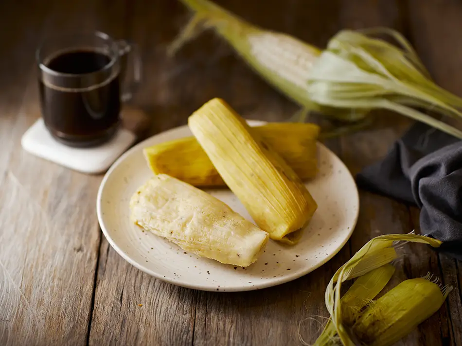 Steamed humitas in corn husks, among traditional Ecuador dishes, show cheese peeking out.