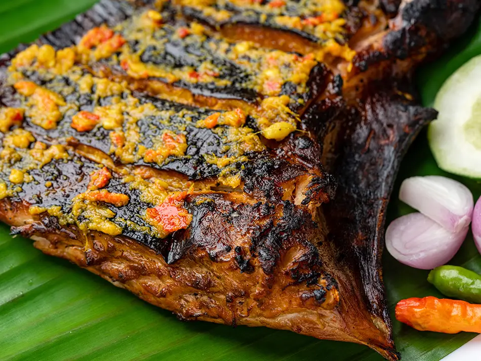 Charcoal-grilled ikan bakar wrapped in banana leaf with tangy dipping sauce.