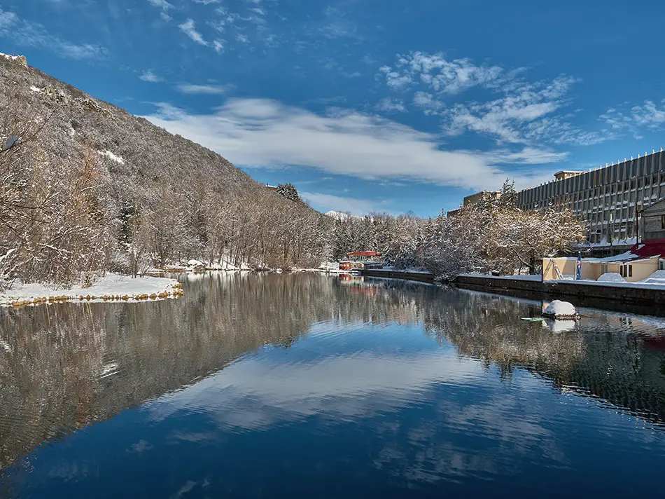 Still water reflecting houses and snowy banks on a bright winter day in Jermuk.