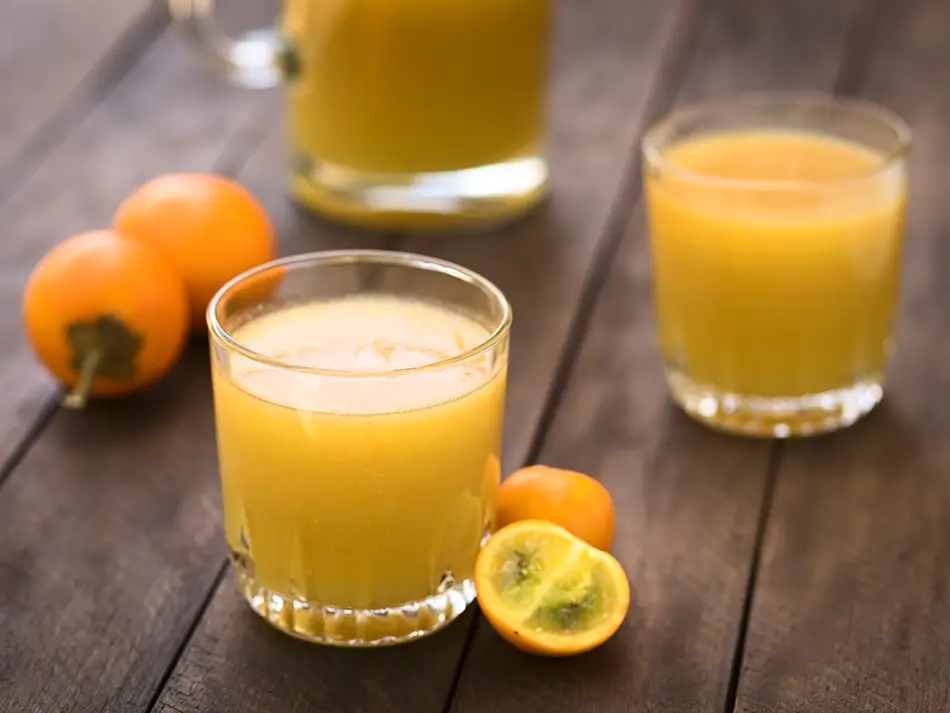 Glasses of bright naranjilla juice with whole fruit on a rustic wooden table.