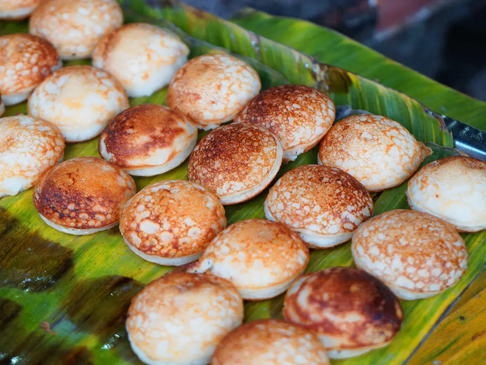Mini coconut rice pancakes on a cast-iron griddle, crisp edges and soft custardy centers.