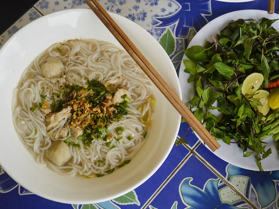 Chewy hand-cut khao piak sen noodles in clear broth with herbs, best dishes in Laos.