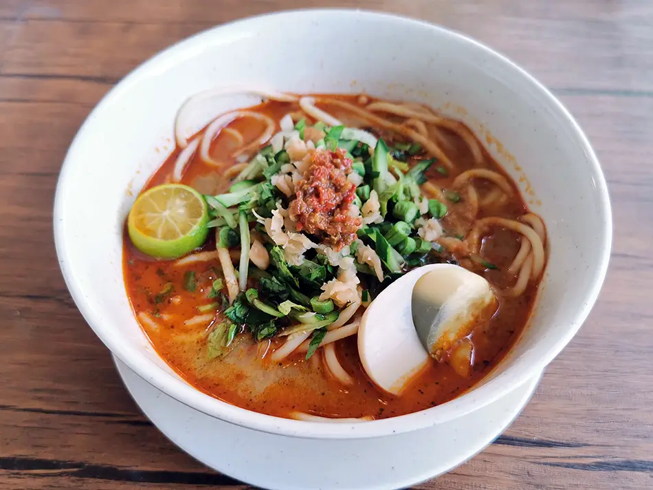 Spaghetti laksa Johor in rich fish gravy garnished with fresh herbs and vegetables.