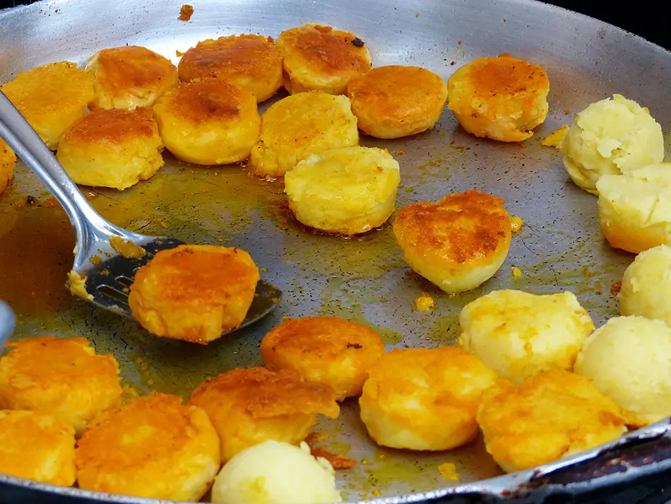 Golden llapingachos, a Best food in Ecuador favorite, with peanut sauce and sausage on a griddle.