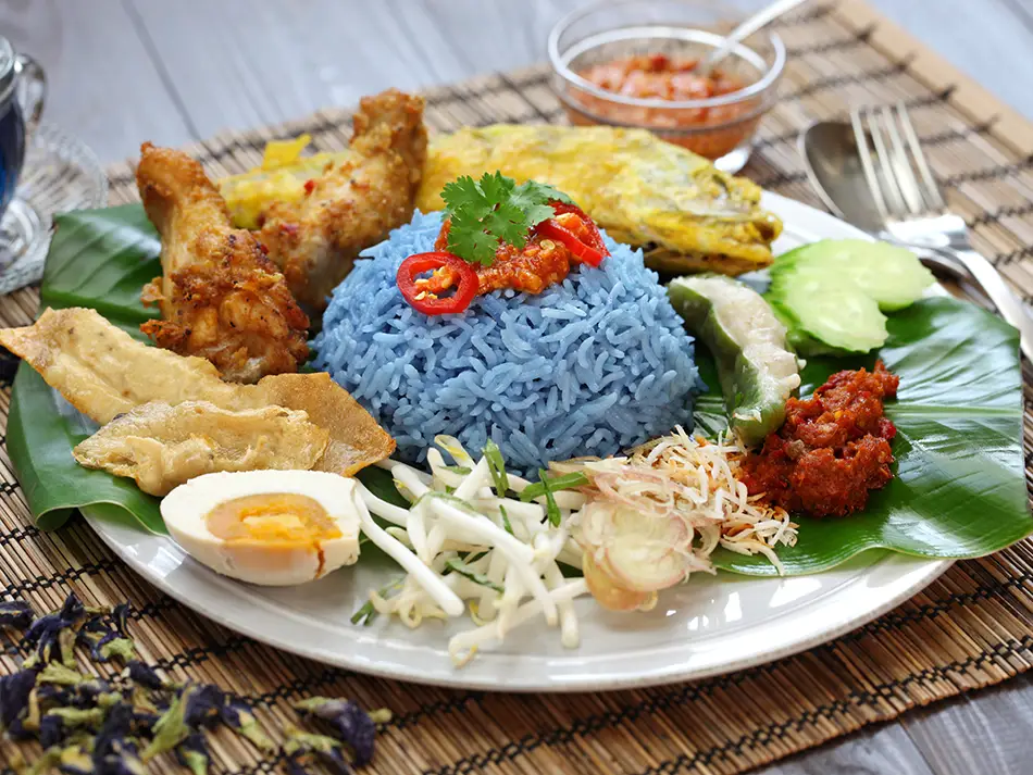 Blue rice nasi kerabu with fresh herbs and fish crackers on a plate.