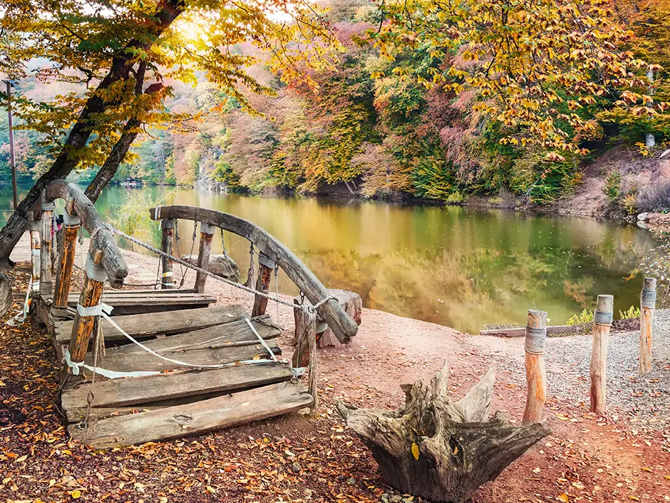 Wooden footbridge over Parz Lake with autumn trees in Dilijan National Park.