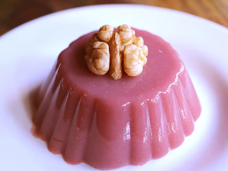 Pelamushi grape pudding molded and topped with a walnut half.