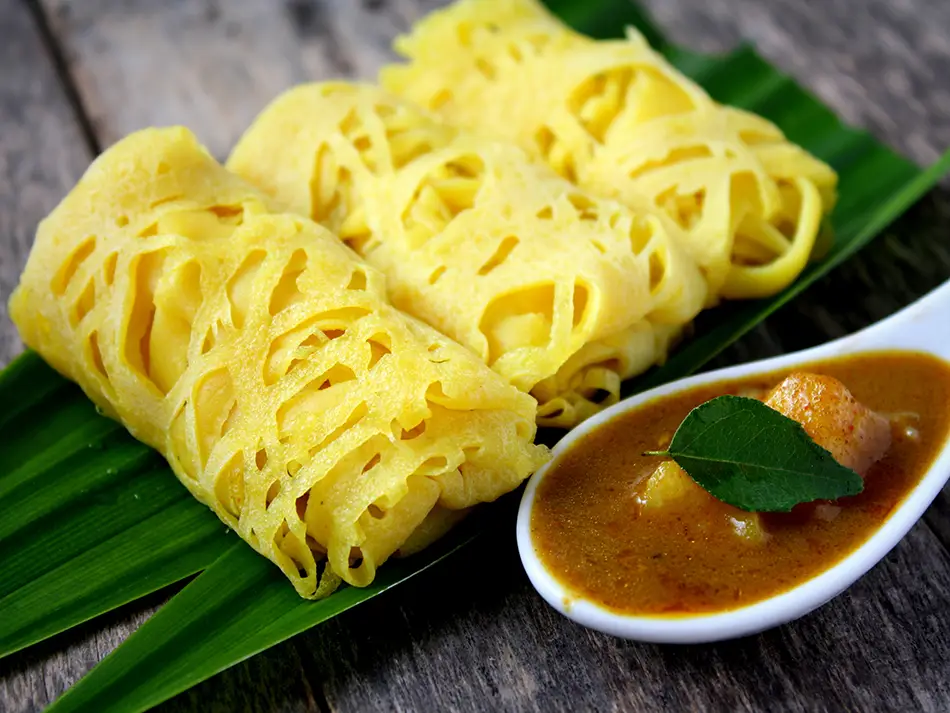 Golden roti jala lace pancakes folded beside a bowl of chicken curry.