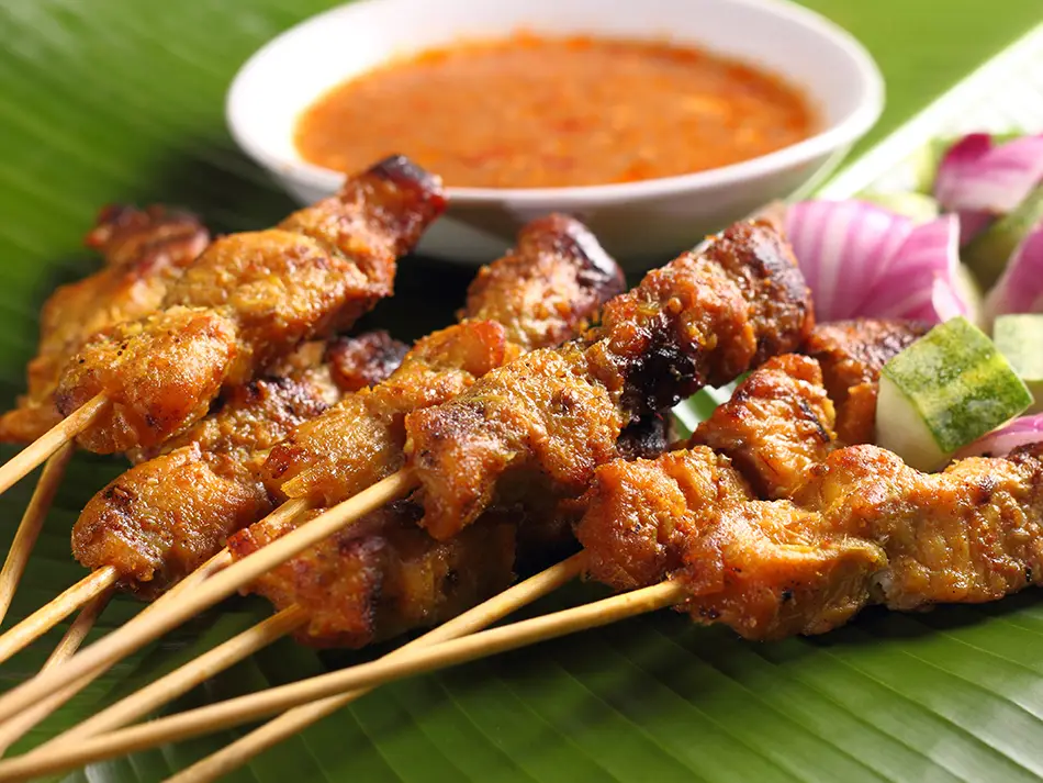 Skewers of satay with peanut sauce and ketupat rice cakes, one of the most famous Malaysia foods.