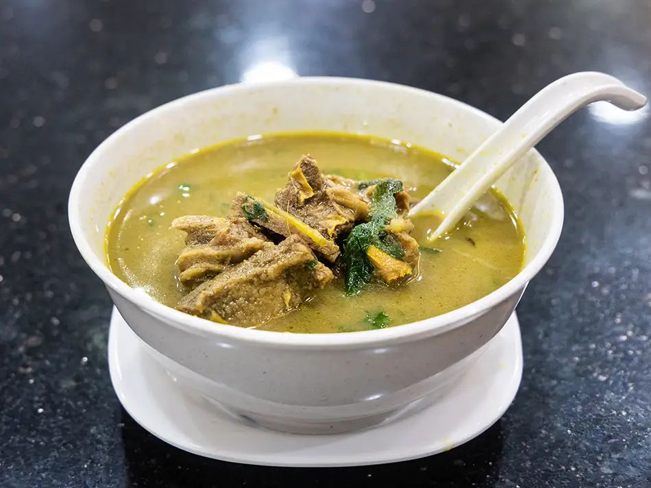 Sup kambing mutton soup with fresh herbs and fried shallots, an iconic Malaysian food.