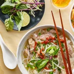 Best food in Vietnam shown in an overhead flat lay of bánh mì, bánh xèo, bún chả, cá kho tộ and more.