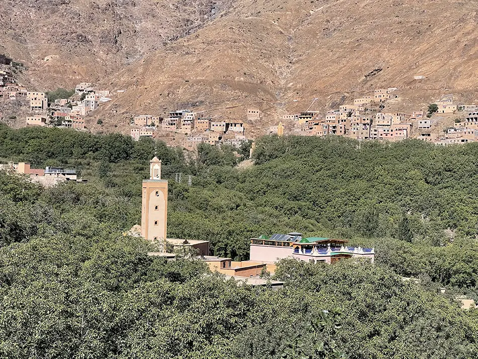 Wide valley panorama with stone village and orchards framed by rugged mountains.