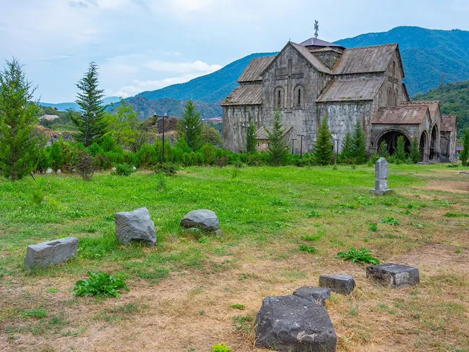 Church and fortress walls rise behind scattered stones on a meadow after rain.