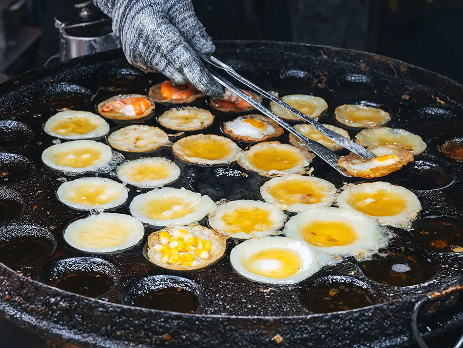 Bite-sized bánh khọt pancakes with shrimp sizzling on a cast-iron pan.